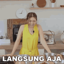 a woman in a yellow dress is standing in a kitchen with the words langsung aja written on the bottom