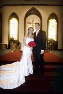 a bride and groom pose for a picture in front of a crucifix