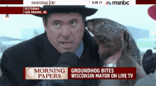 a man is holding a groundhog in front of a msnbc advertisement