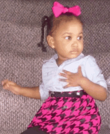 a little girl wearing a pink bow on her hair is sitting on a couch .