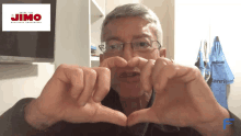 a man making a heart shape with his hands in front of a jimo sign