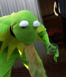 a person dressed as kermit the frog is holding a cup of liquid