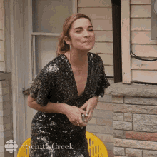 a woman in a sequined dress is sitting in front of a brick building with # schitts creek written on the bottom