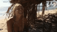 a woman in a bikini is sitting under a palm tree on a beach and smiling .