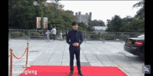 a man in a suit stands on a red carpet in front of a car with the words " bolengling " on the bottom