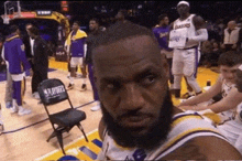 a basketball player with a beard is sitting in a chair on a court .