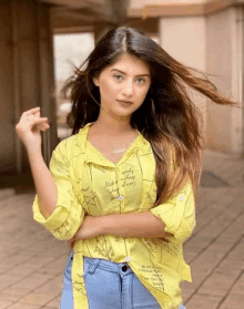 a young woman wearing a yellow shirt and blue jeans is standing with her arms crossed .