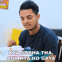 a young man is sitting at a table with a plate of food and a sign that says yummy dhaba