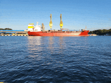 a large red ship is floating in the water with a yellow crane in the background