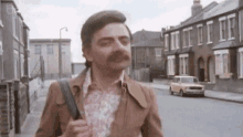 a man with a mustache is walking down a street holding a backpack .