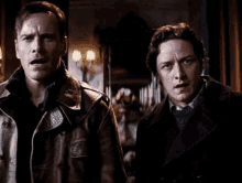 two men in leather jackets are standing next to each other in a dark room .