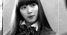 a black and white photo of a young woman wearing a school uniform and a bow tie .