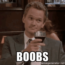 a man in a suit is holding a glass of wine and says boobs .