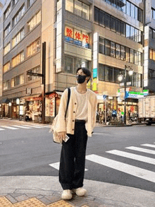 a man wearing a mask and a cardigan is standing in front of a building on a city street .