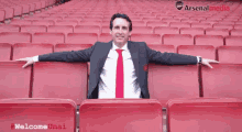 a man in a suit and tie sits in an empty stadium with arsenal media written on the bottom right