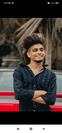 a young man standing in front of a red car with his arms crossed and smiling