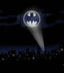 a spotlight is shining on the batman logo in the night sky over a city .