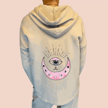 a person wearing a tan hoodie with a pink crescent moon and an eye on it