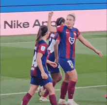 a group of female soccer players are celebrating a goal on a field with a nike ad in the background