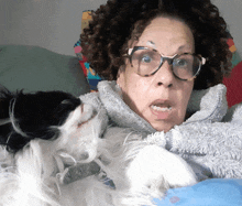 a woman wearing glasses holds a black and white dog in her lap