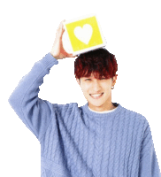 a man wearing a blue sweater is holding a yellow block with a heart on it on his head .