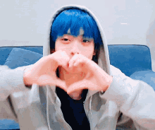 a young man with blue hair is making a heart shape with his hands