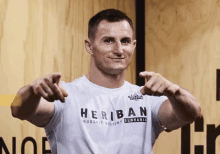 a man wearing a heriban crossfit destiny slovakia shirt is pointing at the camera