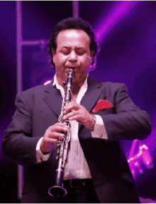 a man in a suit plays a clarinet in front of purple lights