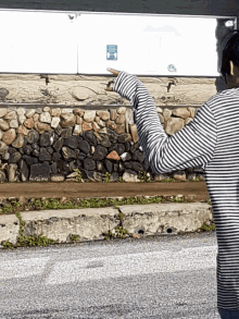 a person standing in front of a stone wall pointing to a sign that says ' a ' on it