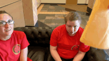 two people sitting on a couch with one wearing a red shirt with a laurel leaf on it