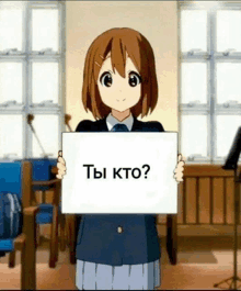 a girl is holding a sign that says `` ты кто ? '' in a classroom .