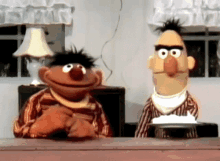 sesame street characters ernie and bert sit at a table with a plate of food