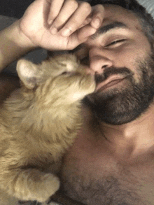 a man with a beard is laying down with a cat on his face