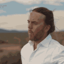 a man with a beard wearing a white shirt is standing in a field