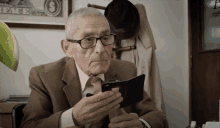 an older man looking at a cell phone in front of a framed dollar bill that says peace on it