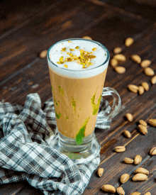 a glass of coffee with pistachios on top and nuts around it