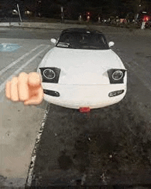 a white sports car is parked in a parking lot with a finger pointing at it .