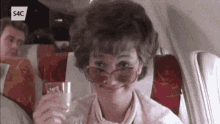 a woman wearing sunglasses is sitting on an airplane holding a glass