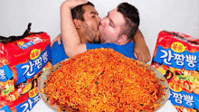 two men are kissing over a pile of noodles on a plate .