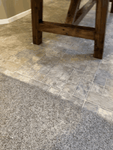 a wooden table sits on a tile floor next to a carpet