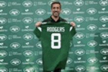 a man is holding a green jersey that says rodgers 8 .