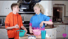 a boy and a girl are preparing food in a kitchen and the girl is wearing a tie dye sweater