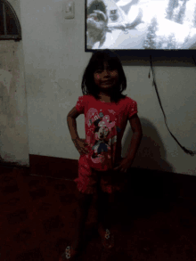 a little girl wearing a minnie mouse shirt stands in front of a flat screen tv