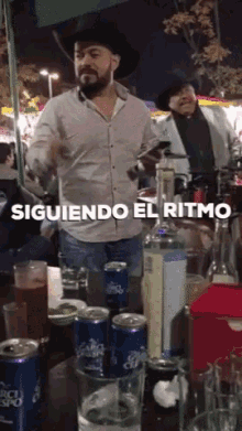 a man in a cowboy hat is dancing in front of a table full of drinks and cans of tropicana