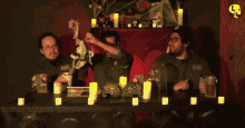 three men are sitting at a table with candles and a mug that says eptv