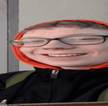 a young boy wearing glasses and an orange hoodie smiles