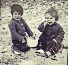 two children are playing in the sand with a bowl