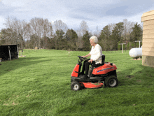 an elderly woman is riding a lawn mower in a lush green yard