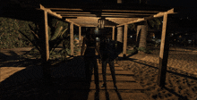 a man in a suit and a woman in a crop top walk under a pergola