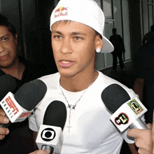 a man wearing a red bull hat is surrounded by a bunch of microphones